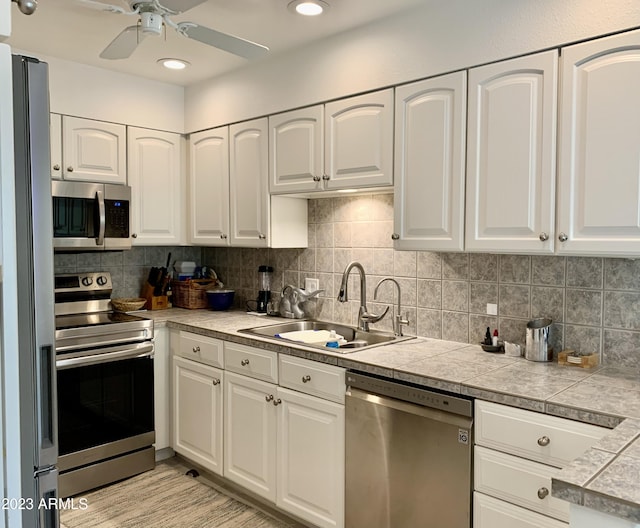 kitchen with appliances with stainless steel finishes, a sink, a ceiling fan, and white cabinetry