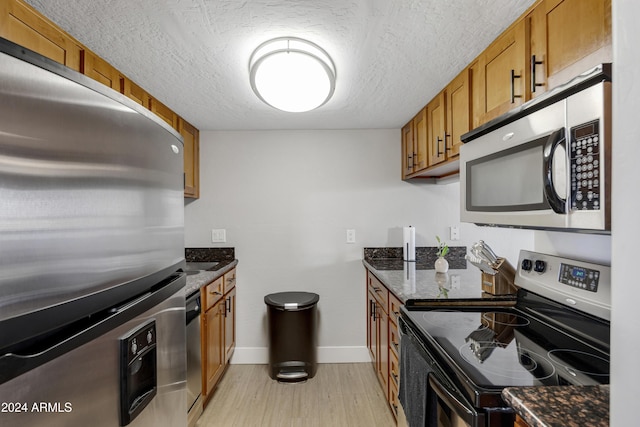 kitchen featuring a textured ceiling, light wood-type flooring, stainless steel appliances, and dark stone counters