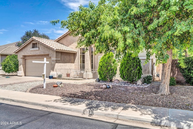 view of property hidden behind natural elements featuring a fenced front yard, a tile roof, stucco siding, concrete driveway, and a garage