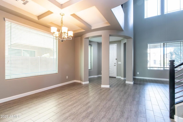 spare room with beamed ceiling, coffered ceiling, a chandelier, and hardwood / wood-style floors