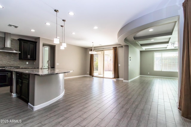 kitchen with sink, a kitchen island with sink, plenty of natural light, decorative backsplash, and wall chimney exhaust hood