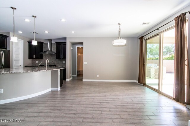 kitchen featuring wall chimney exhaust hood, light stone counters, wood-type flooring, stainless steel refrigerator, and decorative backsplash