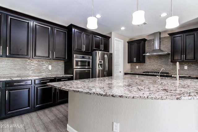 kitchen featuring backsplash, stainless steel appliances, decorative light fixtures, and wall chimney range hood