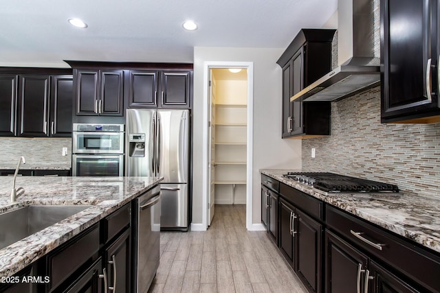 kitchen with tasteful backsplash, stainless steel appliances, light wood-type flooring, and wall chimney range hood