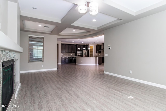 unfurnished living room featuring coffered ceiling, hardwood / wood-style floors, a tile fireplace, and beamed ceiling