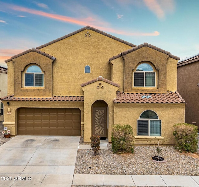 mediterranean / spanish home with a tile roof, concrete driveway, a garage, and stucco siding