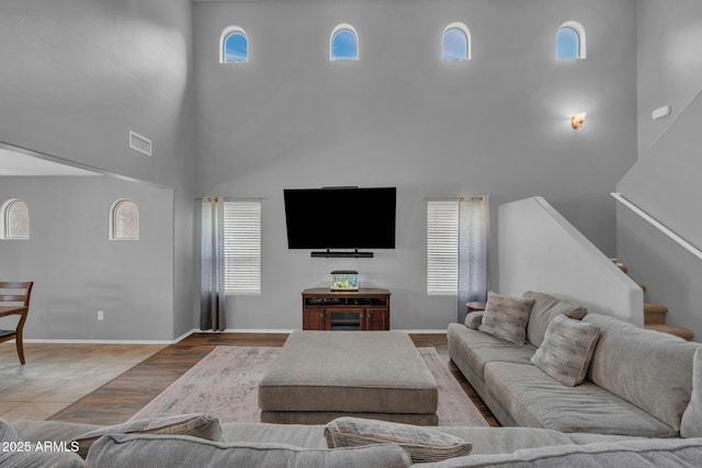 living area featuring visible vents, wood finished floors, a high ceiling, baseboards, and stairs