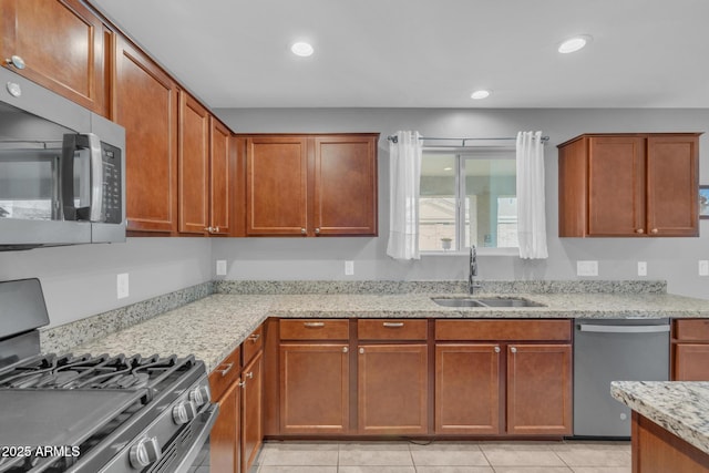 kitchen with a sink, light stone counters, recessed lighting, appliances with stainless steel finishes, and brown cabinetry