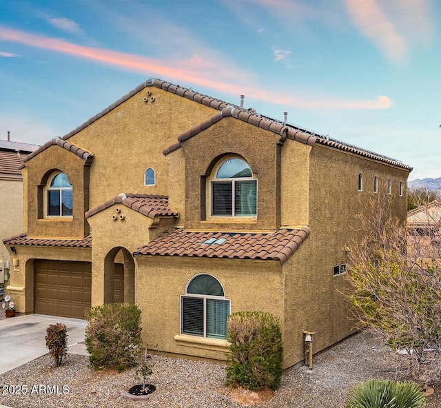 mediterranean / spanish-style house with stucco siding, driveway, a tile roof, and a garage