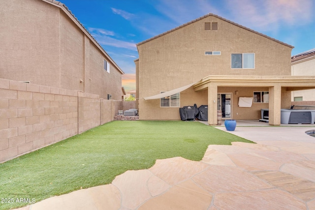 rear view of house featuring a patio, a yard, a fenced backyard, and stucco siding