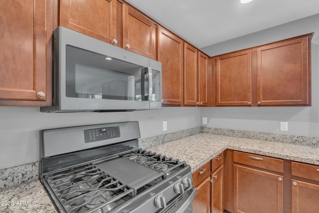 kitchen with light stone countertops, brown cabinets, and stainless steel appliances