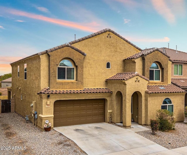 mediterranean / spanish-style home with fence, a tile roof, stucco siding, a garage, and driveway