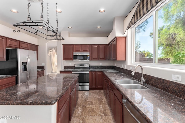 kitchen with sink, decorative light fixtures, dark stone counters, and appliances with stainless steel finishes