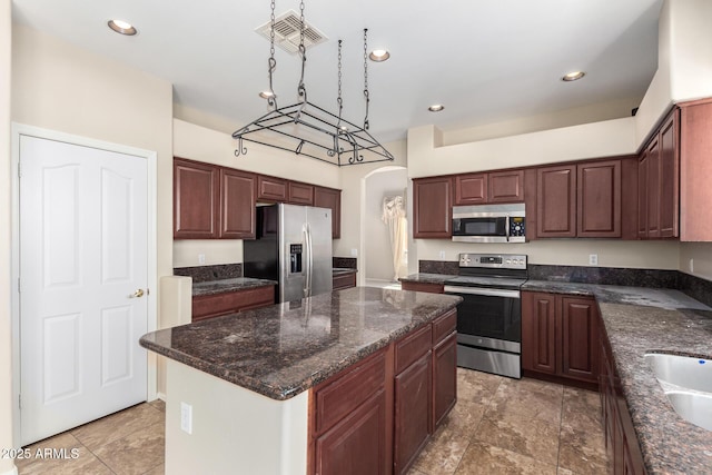 kitchen featuring sink, decorative light fixtures, dark stone counters, a kitchen island, and stainless steel appliances