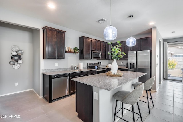 kitchen with dark brown cabinetry, light stone counters, a center island, hanging light fixtures, and appliances with stainless steel finishes