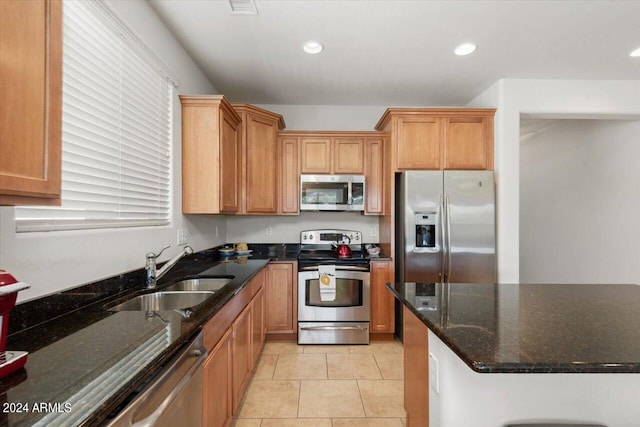 kitchen featuring dark stone countertops, light tile patterned floors, stainless steel appliances, and sink