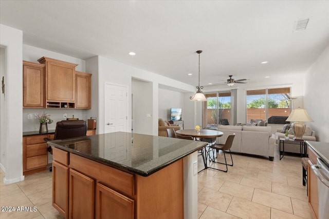 kitchen with ceiling fan, light tile patterned flooring, hanging light fixtures, a kitchen island, and dark stone countertops