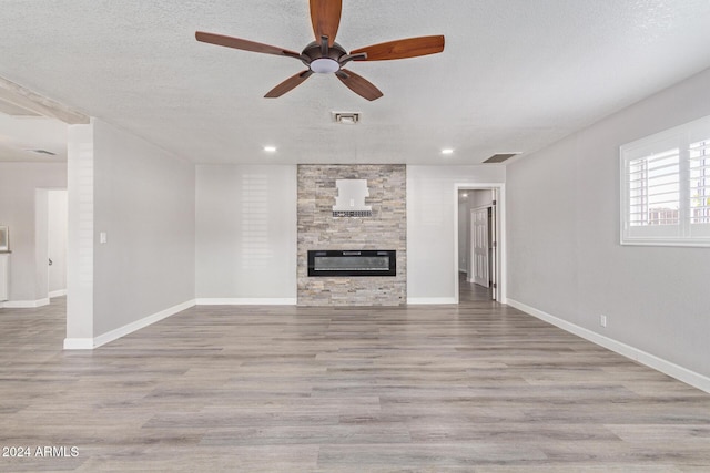 unfurnished living room featuring a fireplace, a textured ceiling, light wood-type flooring, and ceiling fan