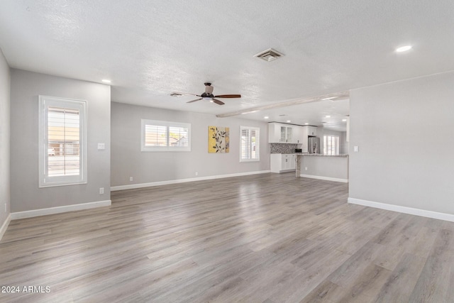 unfurnished living room with ceiling fan, light hardwood / wood-style floors, and a textured ceiling