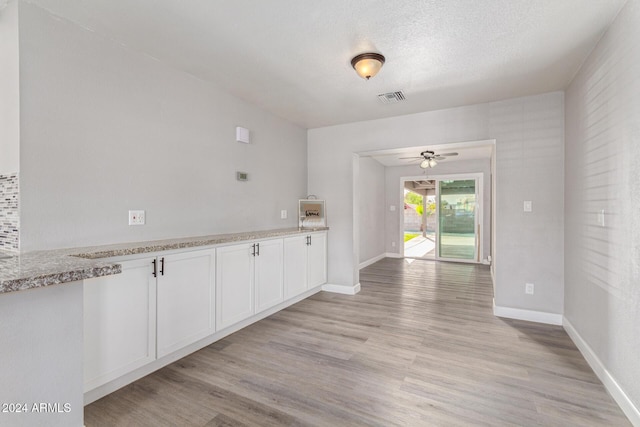 kitchen with white cabinets, ceiling fan, light wood-type flooring, a textured ceiling, and light stone counters