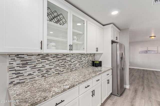 kitchen with light stone countertops, backsplash, stainless steel fridge with ice dispenser, light hardwood / wood-style floors, and white cabinetry