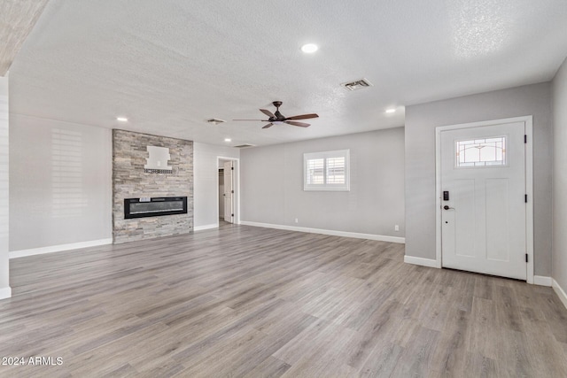 unfurnished living room featuring a fireplace, ceiling fan, light hardwood / wood-style flooring, and a textured ceiling