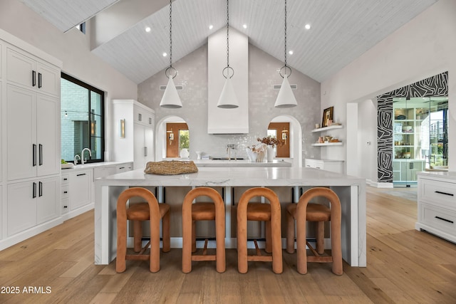 kitchen featuring white cabinetry, decorative light fixtures, a kitchen breakfast bar, a large island, and light stone countertops