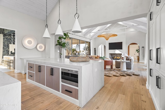 kitchen featuring light stone countertops, a center island, pendant lighting, and light wood-type flooring