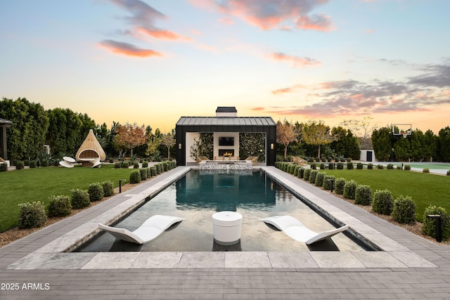 pool at dusk featuring a yard, a patio, an outdoor fireplace, and a gazebo