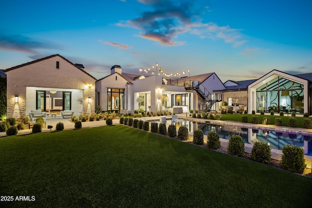 back house at dusk with a balcony, a yard, and a patio area