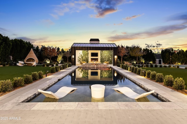 pool at dusk featuring a gazebo, a fireplace, and a lawn