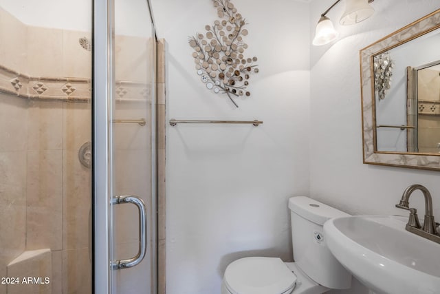 bathroom with toilet, a shower with door, and sink