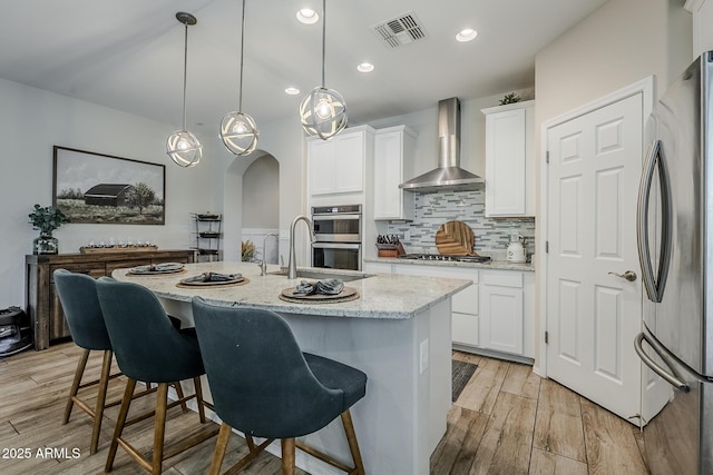 5759 W Saratoga Ct, Florence, AZ 85132 - kitchen featuring appliances with stainless steel finishes, wall chimney exhaust hood, light wood-style floors, decorative backsplash, and white cabinets