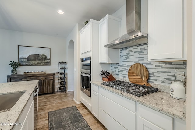 5759 W Saratoga Ct, Florence, AZ 85132 - kitchen with wall chimney range hood, appliances with stainless steel finishes, arched walkways, backsplash, and light stone counters