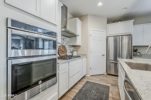 5759 W Saratoga Ct, Florence, AZ 85132 - kitchen featuring appliances with stainless steel finishes, wall chimney exhaust hood, a sink, white cabinets, and decorative backsplash