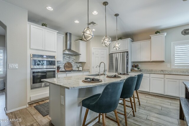 5759 W Saratoga Ct, Florence, AZ 85132 - kitchen with stainless steel appliances, wall chimney exhaust hood, a sink, light wood-type flooring, and white cabinets