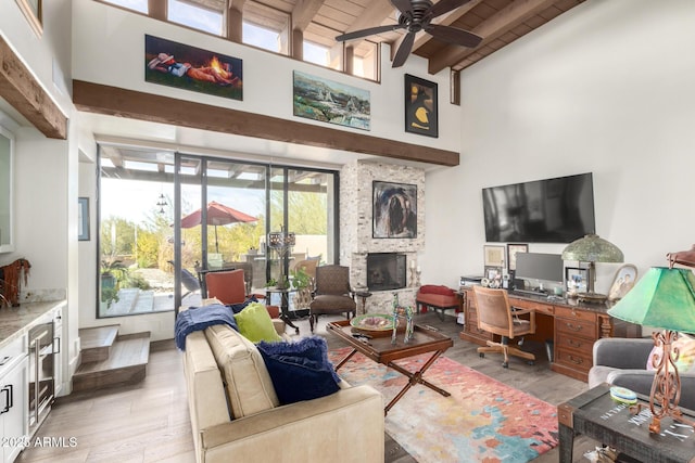 living room featuring light hardwood / wood-style flooring, high vaulted ceiling, a stone fireplace, wooden ceiling, and beamed ceiling