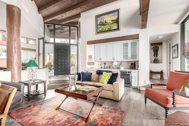 living room with beamed ceiling, wooden ceiling, hardwood / wood-style flooring, beverage cooler, and a high ceiling