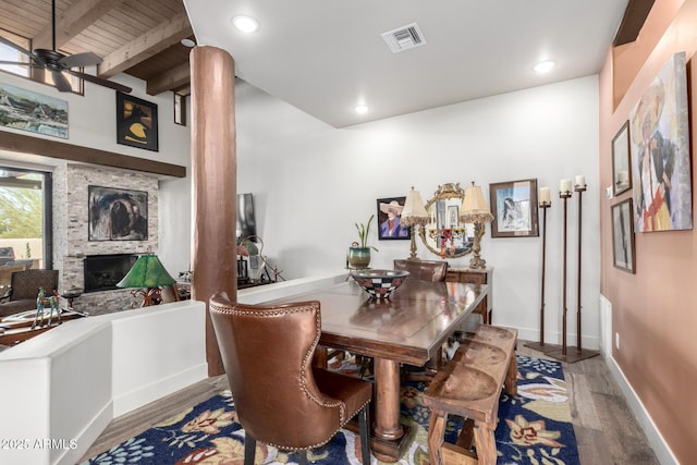 dining room featuring hardwood / wood-style floors, beam ceiling, a fireplace, and ceiling fan