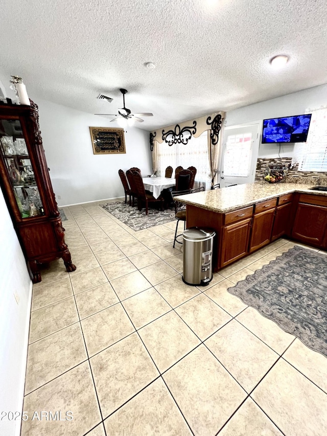 kitchen with ceiling fan, light tile patterned floors, kitchen peninsula, and a textured ceiling