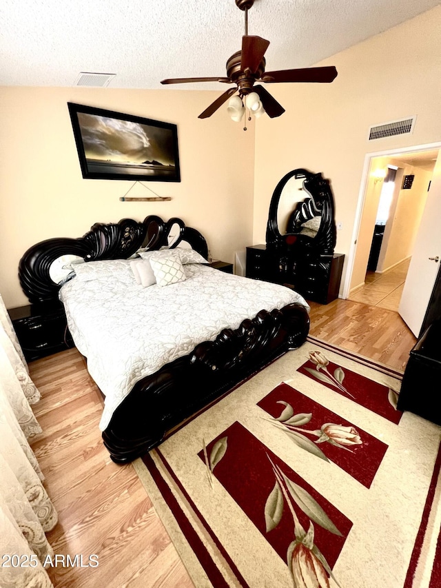 bedroom with vaulted ceiling, ceiling fan, a textured ceiling, and light hardwood / wood-style flooring