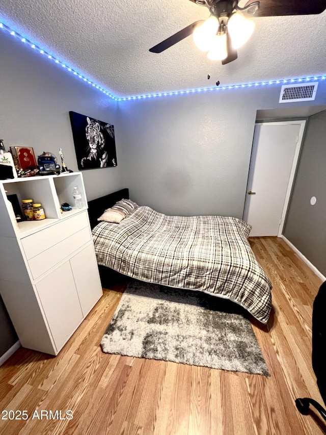 bedroom with a textured ceiling, ceiling fan, and wood-type flooring