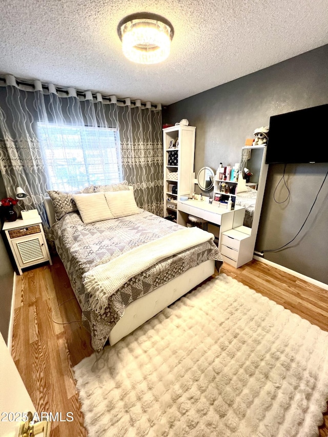 bedroom with a textured ceiling, a wall mounted AC, and wood-type flooring