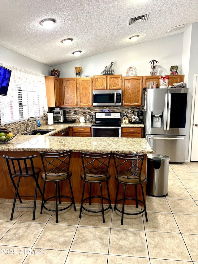 kitchen featuring appliances with stainless steel finishes, lofted ceiling, a kitchen bar, sink, and kitchen peninsula