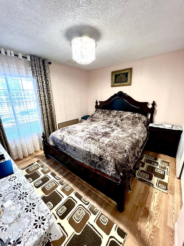 bedroom featuring hardwood / wood-style flooring, a textured ceiling, and an inviting chandelier