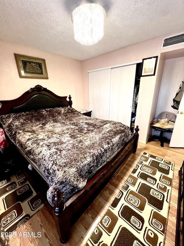 bedroom with a textured ceiling, a closet, wood-type flooring, and an inviting chandelier