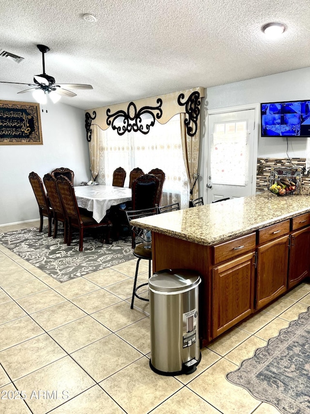 kitchen featuring ceiling fan, light stone countertops, a textured ceiling, and light tile patterned flooring