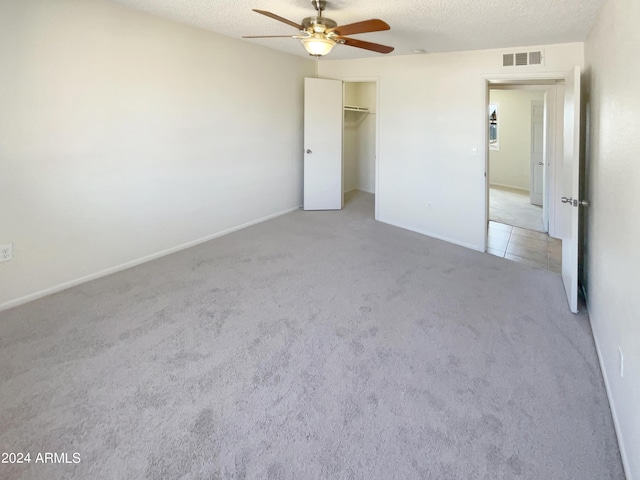 unfurnished bedroom with light colored carpet, a closet, ceiling fan, and a textured ceiling