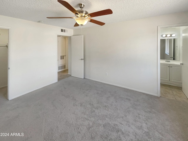 unfurnished bedroom with a textured ceiling, light carpet, sink, and ensuite bath