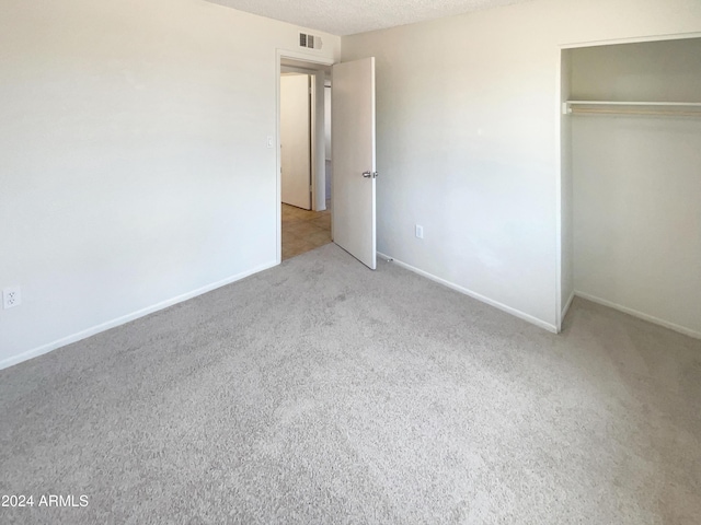 unfurnished bedroom featuring a textured ceiling, light carpet, and a closet